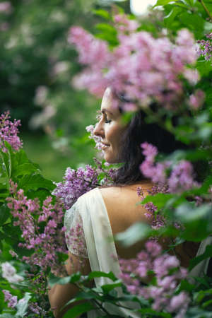 Portrait of an attractive woman surrounded by lilac bushes. Spring and summer, seasonal photos. Vertical photo.の写真素材