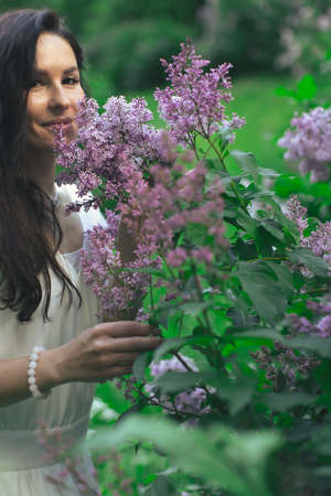 Portrait of an attractive woman surrounded by lilac bushes. Spring and summer, seasonal photos. Vertical photo.の写真素材