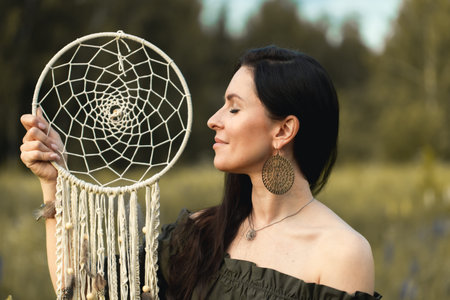 An attractive woman in a summer field with a dream catcher. Front view.