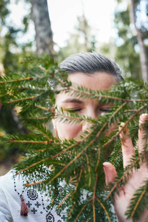 A woman embraces a coniferous tree in the forest. The concept of living in proximity to nature and the forest. Vertical photo.の写真素材