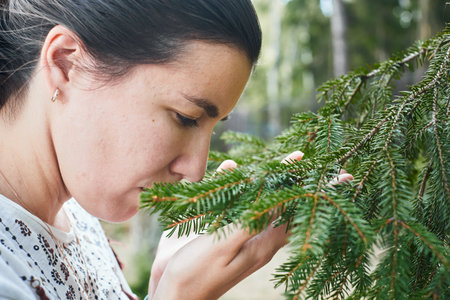 A woman inhales the aroma of a coniferous tree in the forest. Concept of living in proximity to nature and the forest. Front view.の写真素材