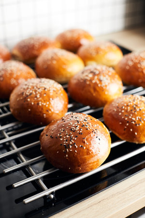 Homemade burger buns with sesame seeds cool on the grill after baking. Vertical photo.