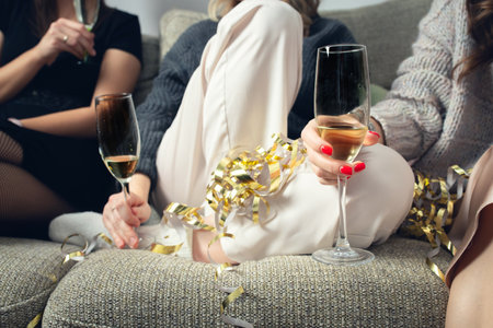 Girls sit on the couch with glasses of champagne, a house party. Front view.の写真素材