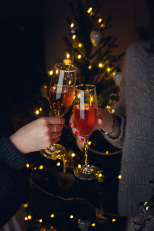 Two girls with glasses of champagne near the Christmas tree for Christmas. Front view. Vertical photo.の写真素材