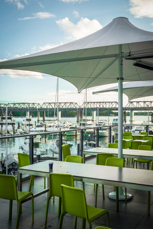 green chairs and white tables are set up near by the yacht dock. the big white umbrella has opened cover the seating. the bridge is far away in the centerの写真素材