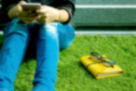 Blurred girl,woman looking at the smartphone sitting in parkの写真素材