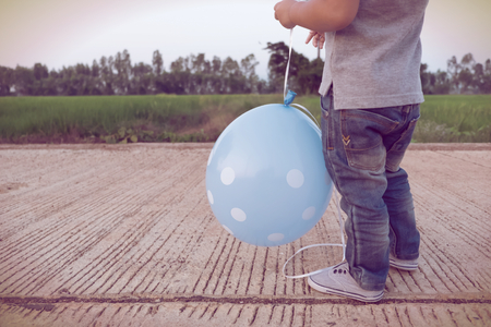Little boy with a blue dot balloons looking at the in spring field green summer landscape, vintage retro styleの写真素材