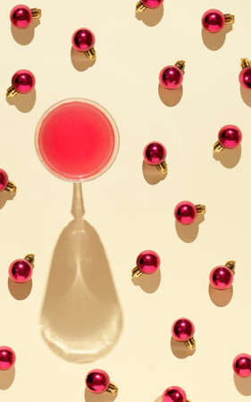 A glass of wine on the table with neatly scattered red christmas decorations on a pastel background. Creative composition xmas. New Year 2022の写真素材