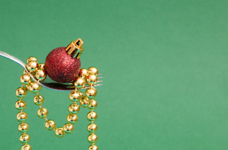 Red Christmas decoration with golden balls on a fork. Green background, xmas minimal creative...