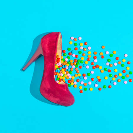 Colorful candies fall out of the red shoes with heels. Minimal creative composition. Copy space, flat lay.の写真素材