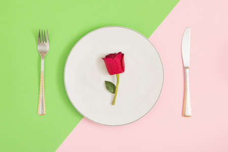 On a colorful table, pastel colors, neatly arranged knife, fork and plate. A red rose was served for the meal. Romantic dinner. Valentine's Day.の写真素材