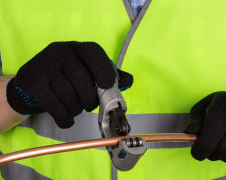 Master in black gloves cutting a copper pipe with a pipe cutter. Isolated on white backgroundの写真素材