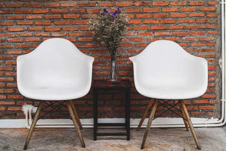 Two white chairs with a table of black vases and flowers were set in front of the red brick wall.の写真素材
