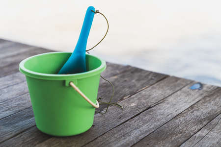 A green plastic bucket for feeding fish and a ladle used to scoop food placed on a wooden bridge by the river.の写真素材