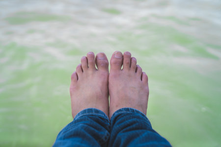 A man wearing long jeans stretching out his feet to the riverの写真素材