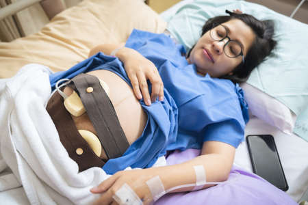 The expectant mother is lying in the hospital bed and is wearing a Fetal Doptone to prepare for the caesarean section.の写真素材
