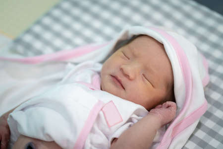A newborn baby is sleeping on her pillow with a blanket wrapped around her body.の写真素材
