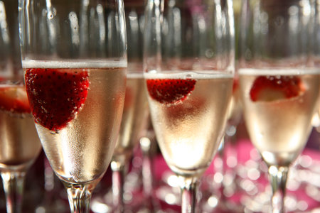Champagne glass with strawberries inside close up with many other glassesの写真素材