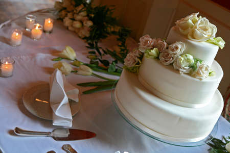 decorated table witha white wedding cake with many peach and white color roses on top, table had roses and candlesの写真素材