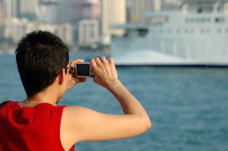 Lady in red shirt taking a picture of a cruise ship with a digital cameraの写真素材