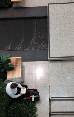 A man reading a book with luggage in the public area of airportの写真素材