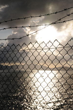 Link fence and barbed wire over sunny sunの写真素材