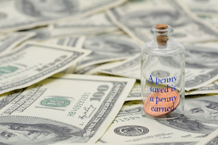 Apenny saved is a penny earned - penny in bottle over US 100 dollar billsの写真素材