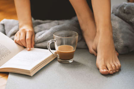 Young girl reading an interesting book and dinking a fresh cup of coffee in her free time.の写真素材