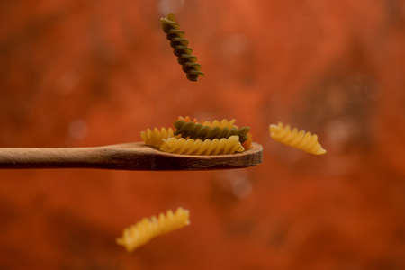 Various mix of dry pasta on wooden spoon. Dry pasta on rustic brown background. Diet and food concept.の写真素材