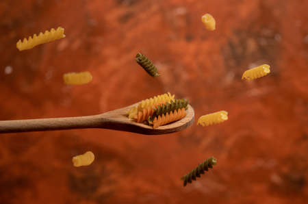 Various mix of dry pasta on wooden spoon. Dry pasta on rustic brown background. Diet and food concept.の写真素材