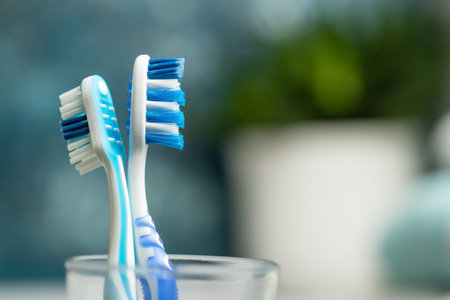 Two toothbrush in a glass surrounded with towels and plants in the bathroom. Health concept.