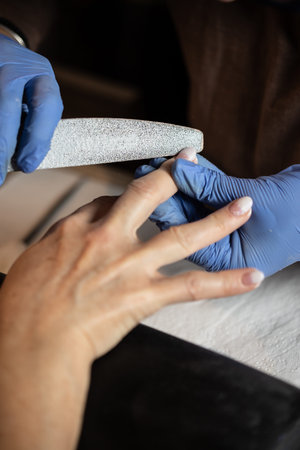 Closeup shot of a woman in a nail salon receiving a manicure by a butician with nail file. Woman...