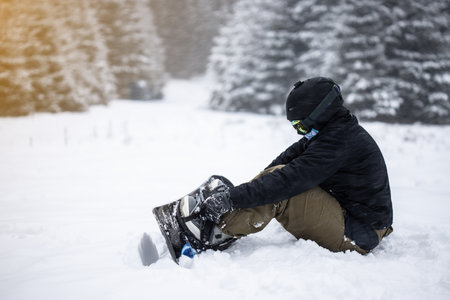 Young girl snowboarder tieing up her snowboard in the snow.の写真素材