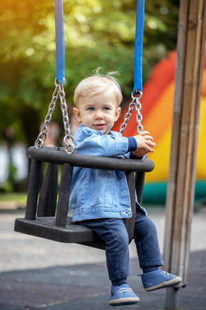 Little blond haired boy swinging on the playground. Happy boy.の写真素材
