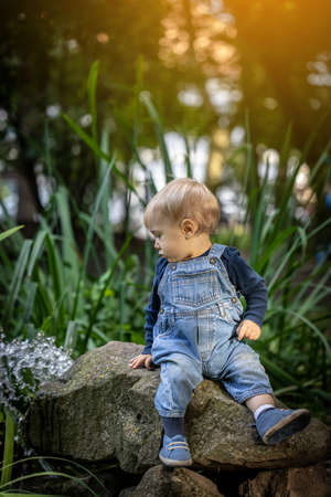 Little blond haired boy sitting in the nature and laughing.の写真素材