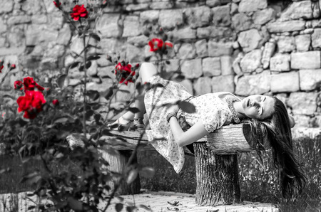 Girl on the bench near wall, black and white shot with red flowersの写真素材