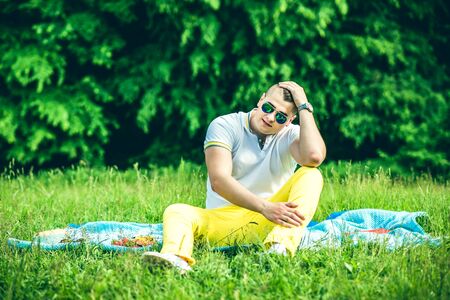 Pretty young man in sunglasses sittin on the grass in the parkの写真素材