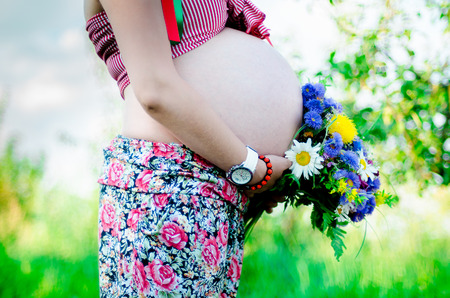 Pragnant happy women outdoor in the garden with flower bouquetの写真素材