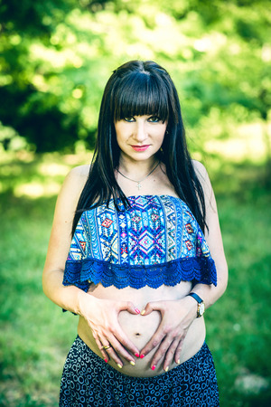 Pregnant woman in the park with heart shaped handsの写真素材