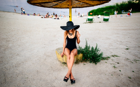 Young pretty girl sitting on the beach in black hatの写真素材