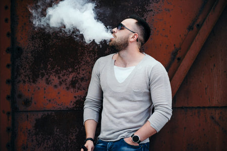 Men with beard vaping outdoor in sunglasses