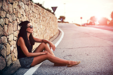 Long hair brunette tourist girl sitting on the roadの写真素材