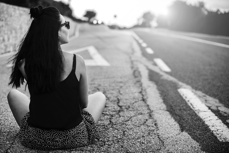 Long hair brunette tourist girl sitting on the roadの写真素材