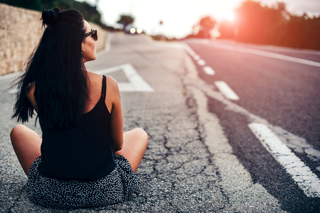 Long hair brunette tourist girl sitting on the roadの写真素材