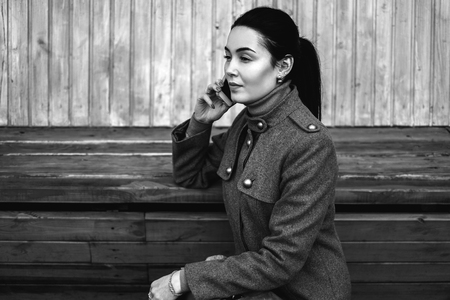Young brunette girl sitting on the bench with mobile phoneの写真素材