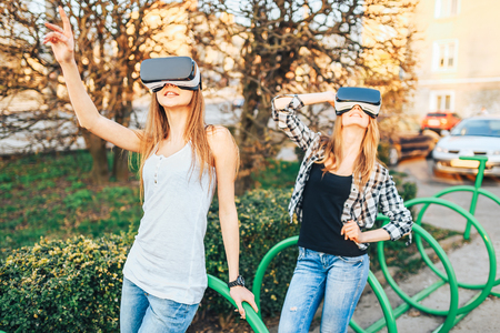 Two young girls enjoy virtual reality glasses outdoorの写真素材