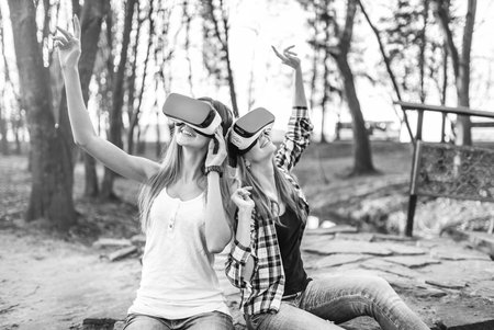 Two young girls enjoy virtual reality glasses outdoor, black and white