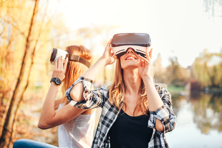 Two young girls enjoy virtual reality glasses outdoorの写真素材