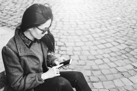 Young brunette girl sitting on the street with cellphone, black and whiteの写真素材