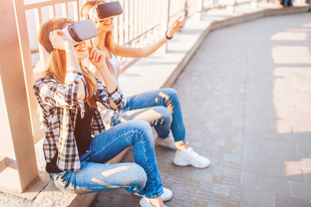 Two young girls enjoy virtual reality glasses outdoorの写真素材